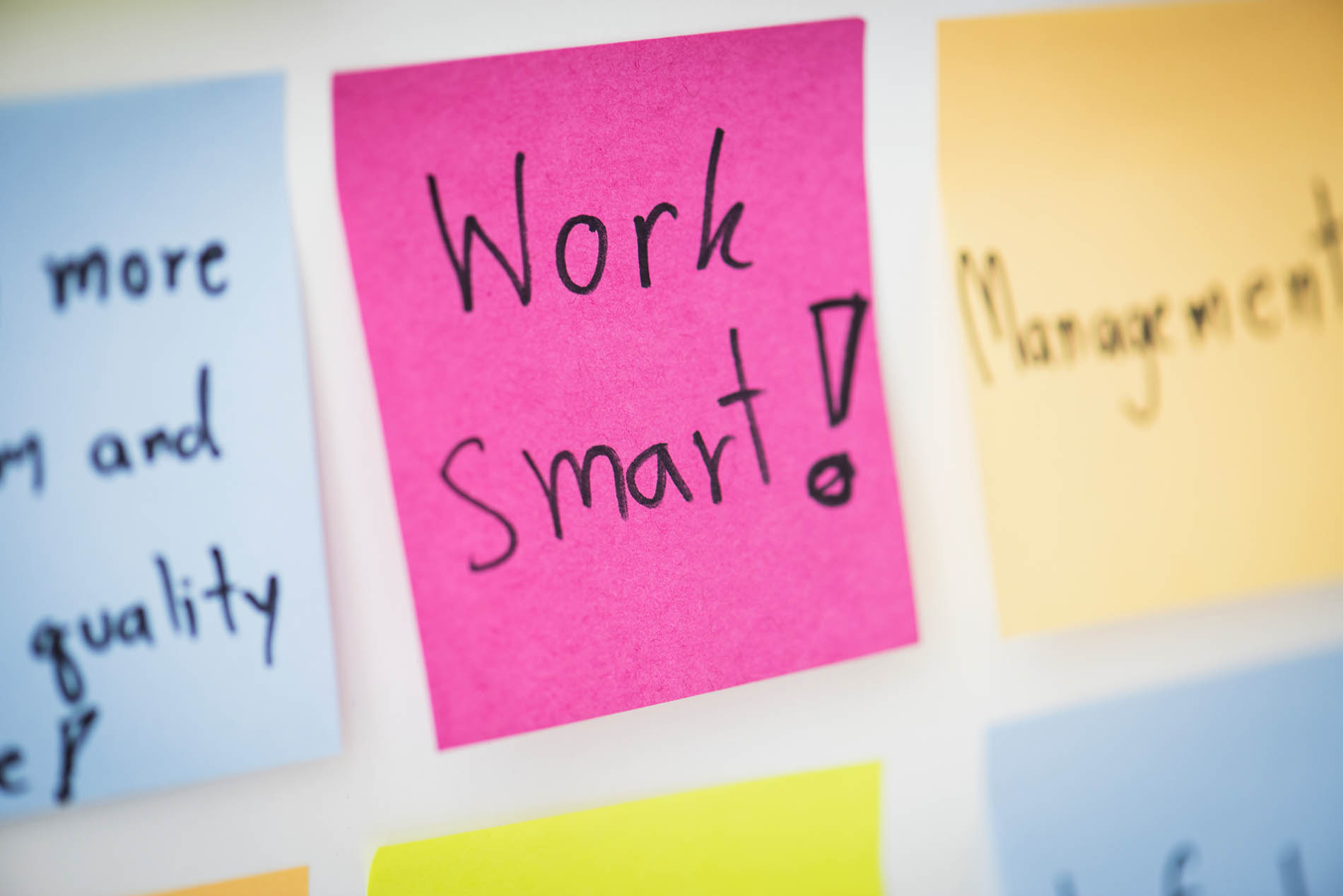 Mehrere bunte Post-Its hängen an einer Pinnwand. In der Mitte hängt ein pinkes Post-It mit der Aufschrift "work smart!"