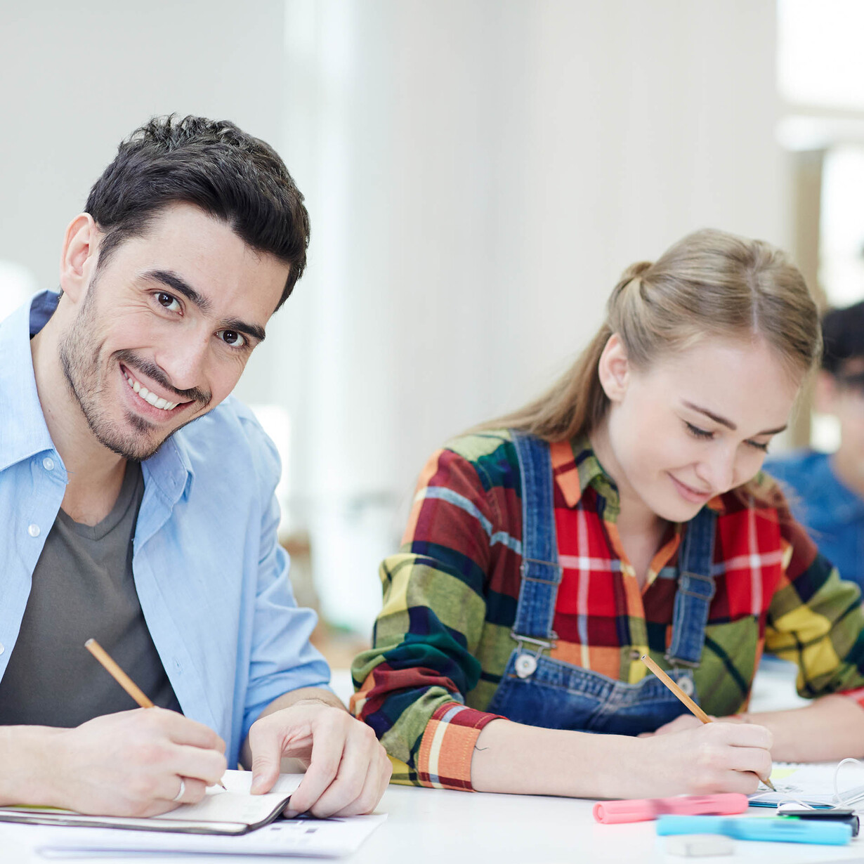 Ein junger Mann und eine junge Frau sitzen mit Schreibblock und Stift an einem Schreibtisch und arbeiten